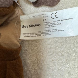 K&ouml;nnte beinhalten: Nahaufnahme eines Pilot Mickey Mouse Pl&uuml;schtiers. Das Spielzeug ist braun, wei&szlig; und beige. Auf dem Etikett steht "Pilot Mickey" und enth&auml;lt das CE-Zeichen. Das Etikett enth&auml;lt auch die Informationen von The Disney Store, Ltd.