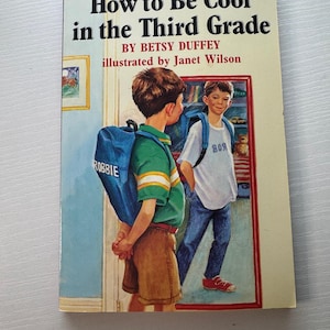 May include: A paperback book titled "How to Be Cool in the Third Grade" by Betsy Duffey, illustrated by Janet Wilson. The cover features a boy with a backpack looking at his reflection. The boy's backpack says "ROBBIE".