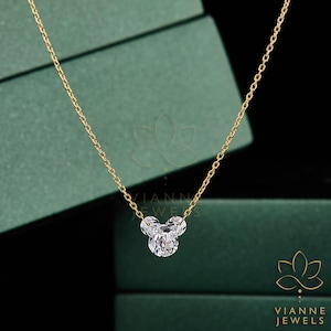 May include: A gold chain necklace with a three-stone pendant. The pendant is made of clear, sparkling stones arranged in a cluster. The necklace is displayed against a green background.