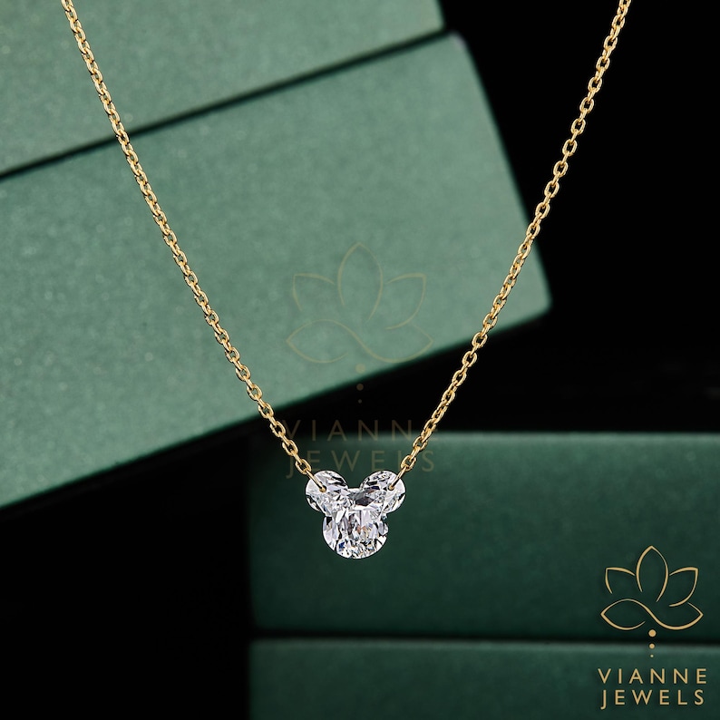 May include: A gold chain necklace with a three-stone pendant. The pendant is made of clear, sparkling stones arranged in a cluster. The necklace is displayed against a green background.