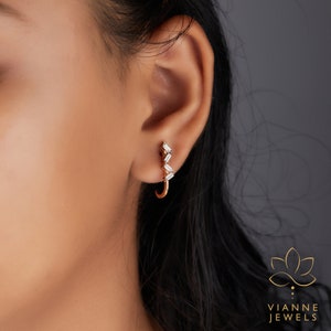 May include: A close-up of a person's ear wearing a gold hoop earring with a row of baguette-shaped diamonds. The earring is a simple and elegant design.