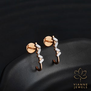 May include: A pair of rose gold hoop earrings with a row of baguette-shaped diamonds set in a zig-zag pattern.  Vianne Jewels.