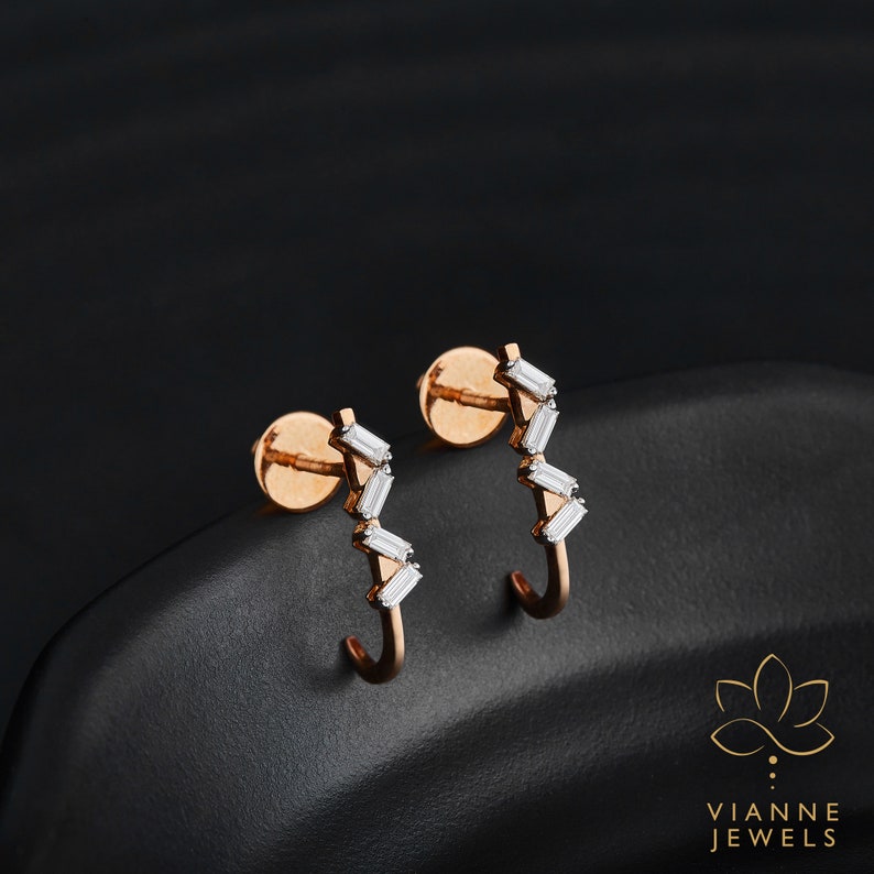 May include: A pair of rose gold hoop earrings with a row of baguette-shaped diamonds set in a zig-zag pattern.  Vianne Jewels.