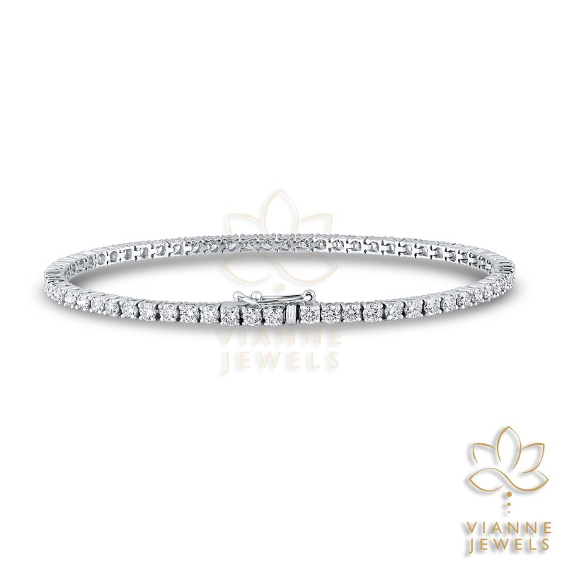 May include: A delicate, silver-toned tennis bracelet featuring a continuous line of small, round, clear gemstones. The bracelet has a secure clasp and is displayed on a white background. The brand name "VIANNE JEWELS" is visible.