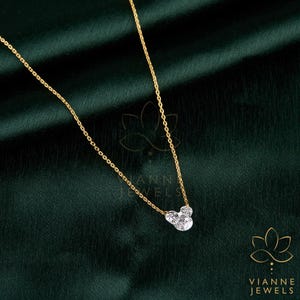 May include: A delicate gold necklace with a pendant shaped like a mouse head, featuring three clear, sparkling stones. The necklace is displayed on a dark green background. The brand name "VIANNE JEWELS" is visible.