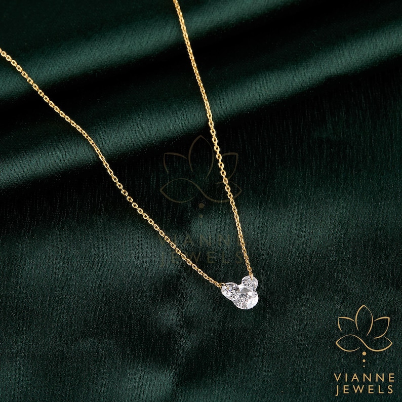 May include: A delicate gold necklace with a pendant shaped like a mouse head, featuring three clear, sparkling stones. The necklace is displayed on a dark green background. The brand name "VIANNE JEWELS" is visible.
