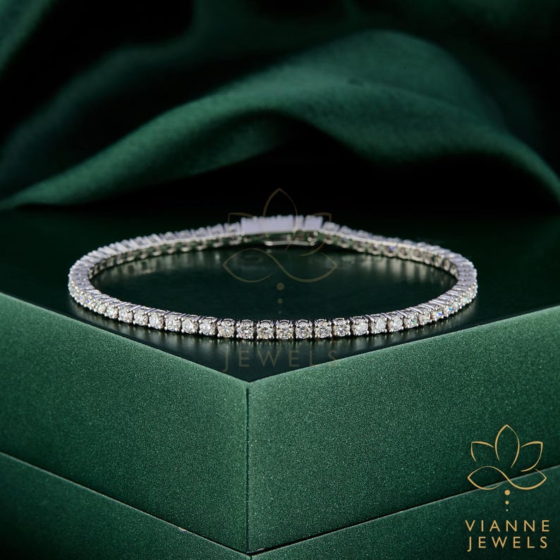 May include: A delicate silver bracelet with numerous small, sparkling gemstones. The bracelet is set against a dark green backdrop, highlighting its brilliance. The bracelet is a tennis style, perfect for adding a touch of elegance to any outfit.