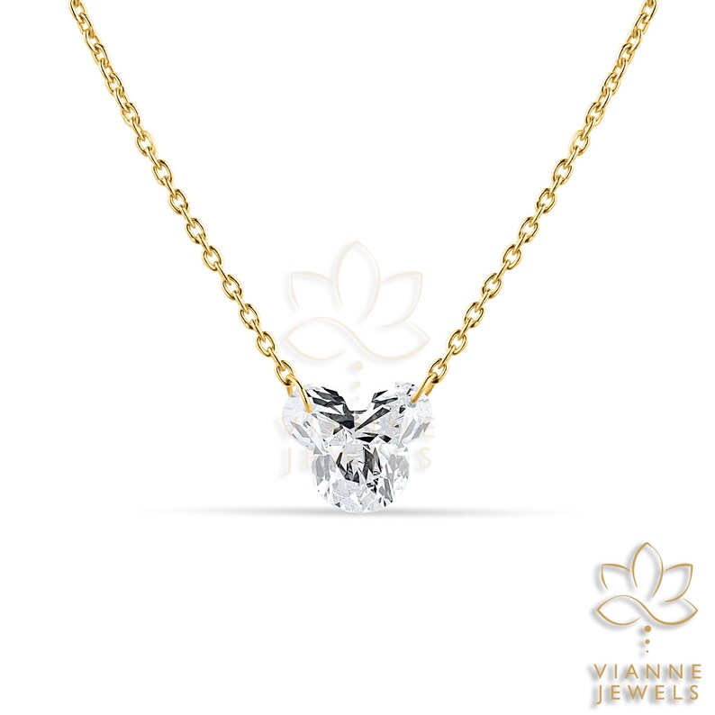May include: A delicate gold chain necklace featuring a heart-shaped diamond pendant. The diamond is clear and faceted, catching the light. The necklace is a simple, elegant piece of jewelry.