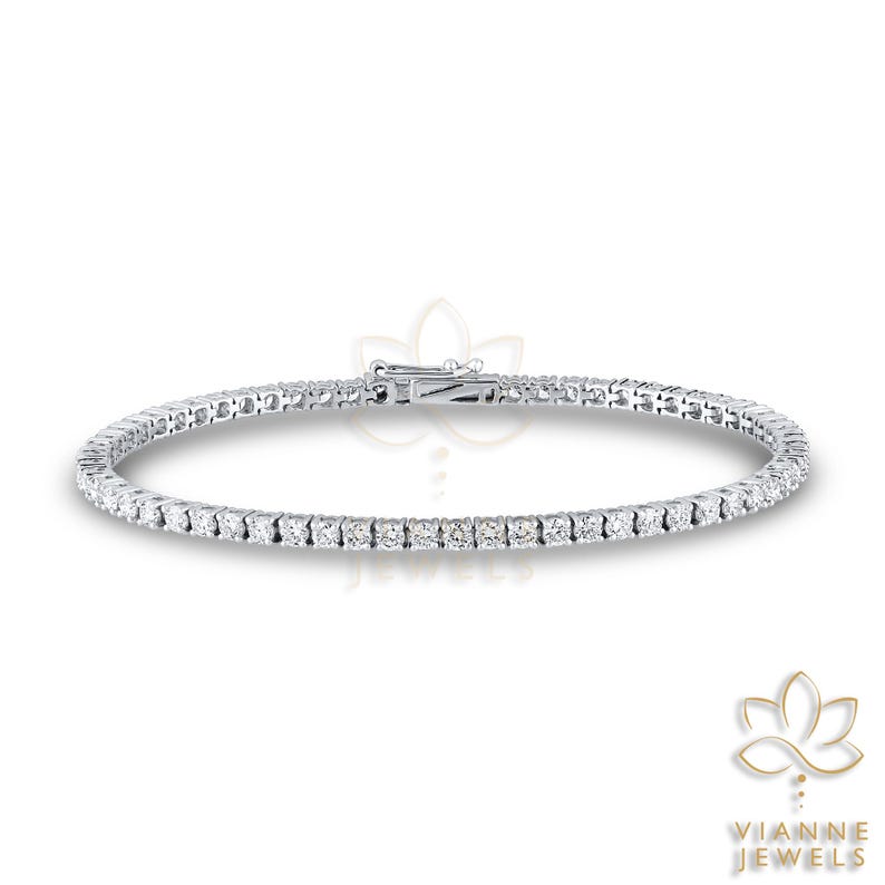 May include: A tennis bracelet featuring a continuous line of round-cut diamonds set in a silver metal. The bracelet is secured with a clasp. The jewelry is from Vianne Jewels.