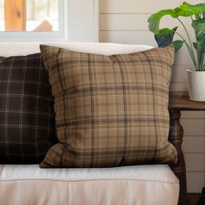 May include: Two throw pillows with a plaid pattern. One pillow is brown and black, and the other is brown and tan.