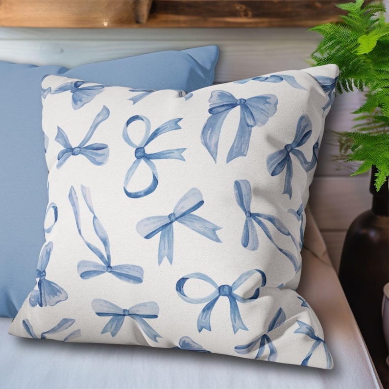 May include: A white pillow with a blue watercolor bow pattern. The pillow is on a light blue pillow and a light brown surface.