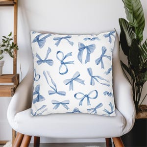 May include: A white throw pillow with a blue watercolor pattern of bows. The pillow is sitting on a white chair.