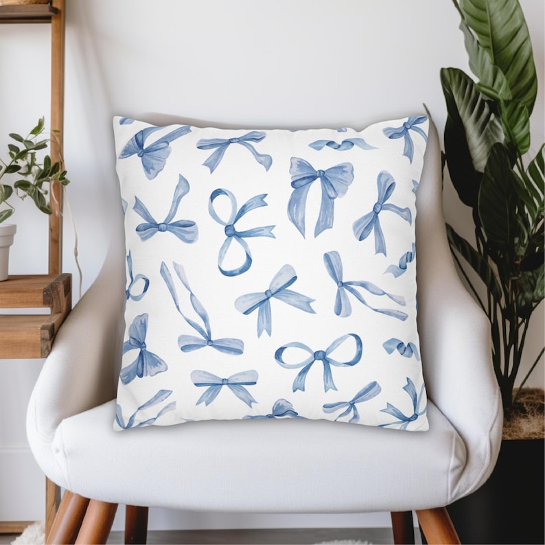 May include: A white throw pillow with a blue watercolor pattern of bows. The pillow is sitting on a white chair.