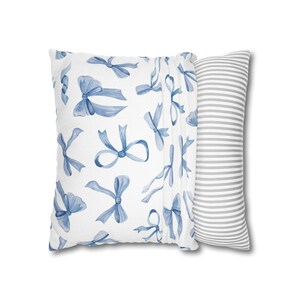 May include: A white pillow with a blue watercolor bow pattern on one side and a gray and white striped pattern on the other side.