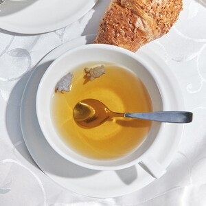 Könnte beinhalten: Eine weiße Teetasse und Untertasse mit einem goldenen Löffel darin. Die Teetasse ist mit hellbraunem Tee gefüllt und hat zwei kleine, schildkrötenförmige Tee-Infuser, die im Tee schwimmen.