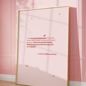 May include: A pink framed poster with a quote from the book "A Court of Mist and Fury" by Sarah J. Maas. The quote reads: "I was burning through books every day, stories about people and places I'd never heard of. They were perhaps the only thing that kept me from teetering into utter despair."