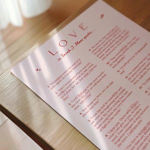 May include: A printed page with the word "LOVE" in red, along with quotes from Sarah J. Maas. The text is on a light pink background. The page is resting on a wooden surface.
