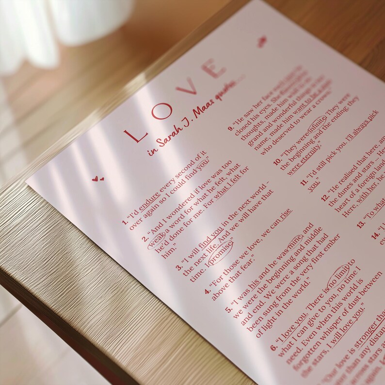 May include: A printed page with the word "LOVE" in red, along with quotes from Sarah J. Maas. The text is on a light pink background. The page is resting on a wooden surface.