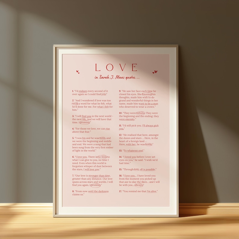 May include: A framed print with the word "LOVE" at the top, followed by a quote from Sarah J. Maas. The text is in a serif font, with a light pink background and a white frame. The print is displayed on a wooden surface.