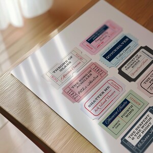 K&ouml;nnte beinhalten: Eine Sammlung von Theaterkarten im Vintage-Stil in Pastellfarben wie Rosa, Blau und Grau. Jede Karte zeigt einen anderen Titel und Veranstaltungsort, gedruckt in dekorativen Schriftarten. Die Karten liegen auf einer wei&szlig;en Oberfl&auml;che.