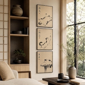 May include: Three framed wall art prints featuring black ink cat illustrations on a beige background. The top print shows a cat lying on its back, the middle shows a cat reaching upward, and the bottom shows a cat sitting on a table.