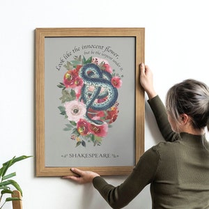 May include: A framed print featuring a watercolour illustration of a snake coiled around pink and red flowers. The quote "Look like the innocent flower, but be the serpent under't" is written in a cursive font. The text "SHAKESPEARE" is written below the illustration.
