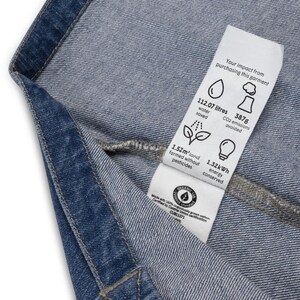 May include: A white tag attached to a pair of blue jeans with the text "Your impact from purchasing this garment" and details about the environmental impact of the garment, including water saved, CO2 emissions avoided, land farmed without pesticides, and energy conserved.