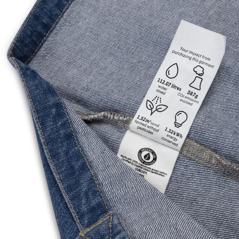 May include: A white tag attached to a pair of blue jeans with the text "Your impact from purchasing this garment" and details about the environmental impact of the garment, including water saved, CO2 emissions avoided, land farmed without pesticides, and energy conserved.