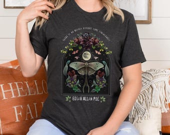 May include: Dark grey t-shirt with a graphic print of a moth, flowers, and a crescent moon. The text "There is no beauty without some strangeness" and "Edgar Allan Poe" are printed on the shirt.