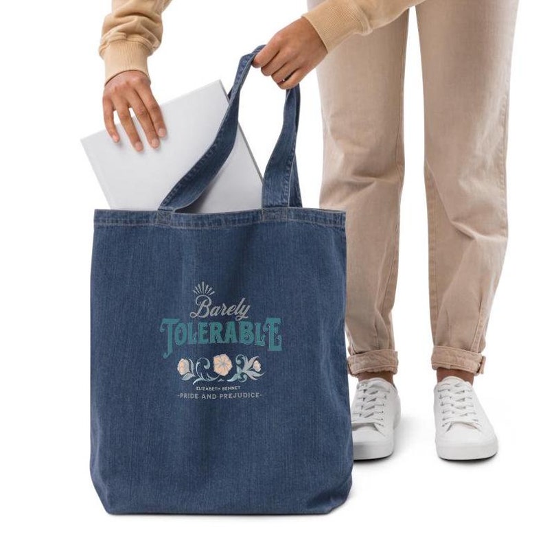 May include: A blue denim tote bag with the text "Barely Tolerable" in a teal and white font. The text is surrounded by a floral design. Below the text is the text "Elizabeth Bennet - Pride and Prejudice".