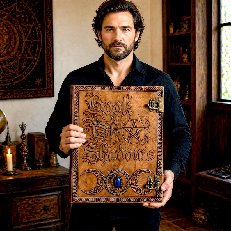 Puede incluir: Un libro encuadernado en cuero marr&oacute;n con el t&iacute;tulo "Book of Shadows" en relieve en la portada. La portada presenta un pentagrama, lunas crecientes y una piedra preciosa azul. El libro tiene cierres met&aacute;licos y bordes decorativos.