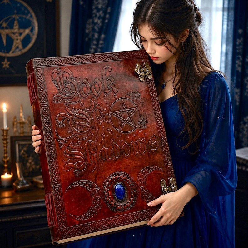 Puede incluir: Un libro grande, de estilo antiguo, con el t&iacute;tulo "Book of Shadows" grabado en la portada. La portada es de un marr&oacute;n rojizo oscuro con dise&ntilde;os intrincados, un pentagrama y una piedra preciosa azul. El libro tiene cierres met&aacute;licos y un borde decorativo.