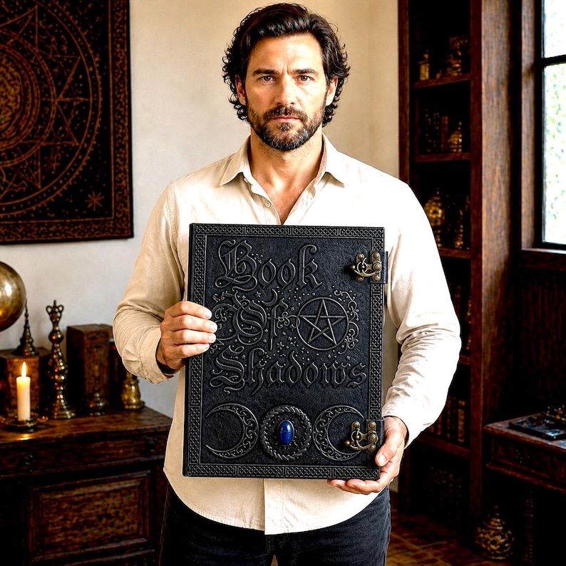 Puede incluir: Libro negro encuadernado en cuero con el t&iacute;tulo "Book of Shadows" en relieve. La portada presenta un pentagrama, lunas crecientes y una gema azul. El libro tiene cierres met&aacute;licos ornamentados.