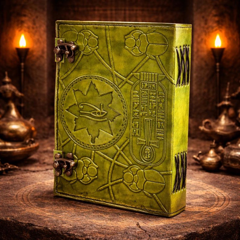 May include: A green leather book with embossed Egyptian hieroglyphs and scarab beetles. The book has metal clasps and decorative stitching along the spine. The cover features an eye symbol within a star.