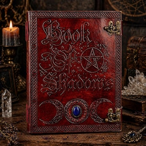 Puede incluir: Un libro encuadernado en cuero rojo titulado "Book of Shadows" con letras en relieve y un dise&ntilde;o de pentagrama. El libro presenta un cierre de broche y una piedra preciosa azul. La portada tiene un borde decorativo.