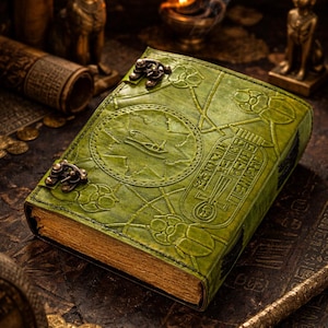 May include: A green leather journal with embossed Egyptian hieroglyphs and symbols. The cover features a circular design and decorative clasps. The aged pages have gold edges. The journal is surrounded by other ancient Egyptian artifacts.