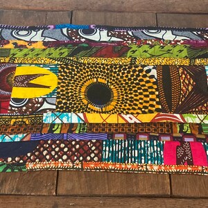 May include: A rectangular patchwork textile with a vibrant mix of African-inspired patterns. The design incorporates various colours, including yellow, blue, red, and green, with geometric and abstract motifs. The edges are neatly finished, showcasing the craftsmanship.