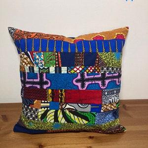 May include: A colourful patchwork cushion featuring a variety of geometric and floral patterns in shades of blue, red, green, yellow, and orange. The cushion is made from fabric scraps sewn together in a random pattern.