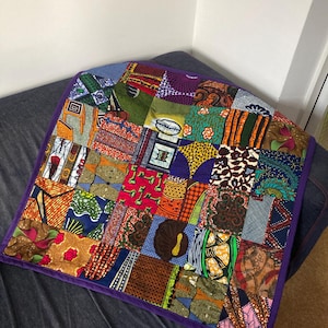 Peut inclure: Une courtepointe patchwork colorée avec une variété de carrés de tissu à motifs dans les tons de rouge, orange, vert et bleu. La courtepointe est bordée d'une bordure violette.