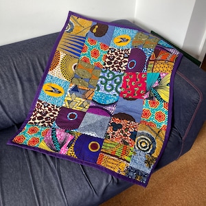 May include: A colorful patchwork quilt with a purple border. The quilt is made of various fabrics with different patterns, including geometric shapes, flowers, and animals.