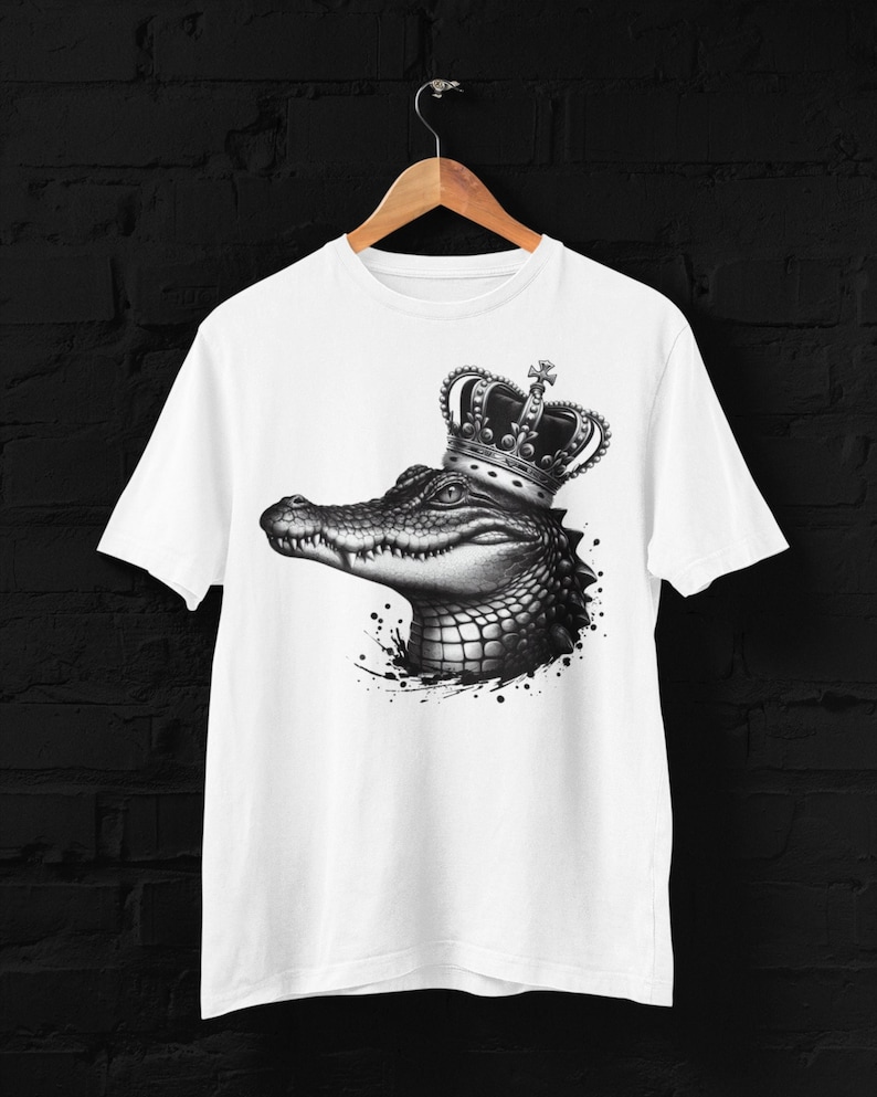 May include: White t-shirt with a black and white illustration of a crocodile wearing a silver crown. The crocodile is facing left and has a detailed, textured design.