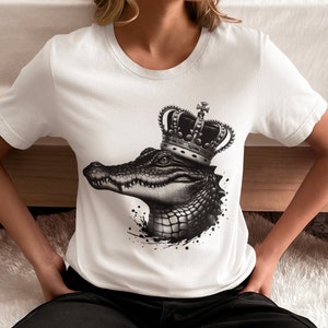 May include: White t-shirt with a black and white graphic of an alligator wearing a gold crown. The alligator is facing the left side of the image.