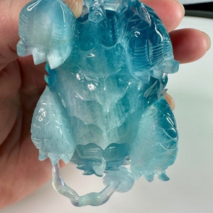 May include: A carved aquamarine turtle figurine with a light blue and white color scheme. The turtle is depicted with its head and legs outstretched.