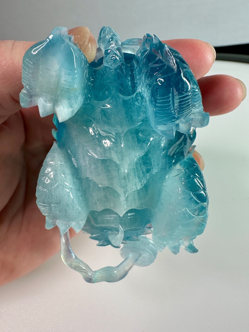 May include: A carved aquamarine turtle figurine with a light blue and white color scheme. The turtle is depicted with its head and legs outstretched.