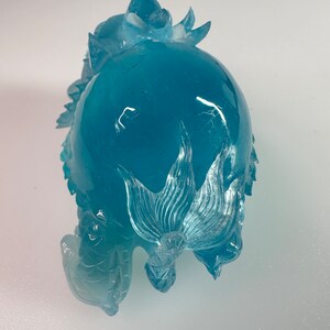 May include: A blue glass sculpture of a dragon with intricate details. The dragon is curled up with its tail wrapped around its body.