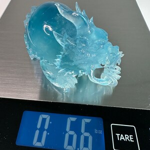May include: A clear blue glass dragon sculpture weighing 0.66 pounds on a digital scale.