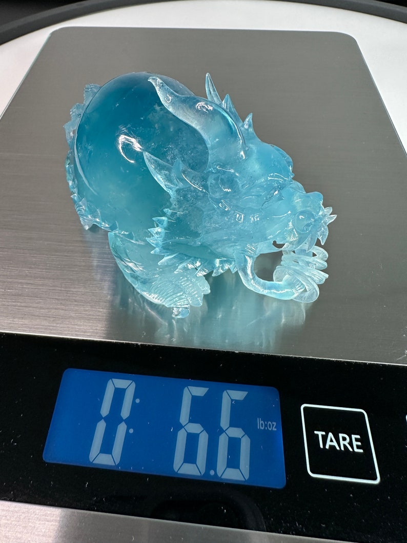 May include: A clear blue glass dragon sculpture weighing 0.66 pounds on a digital scale.