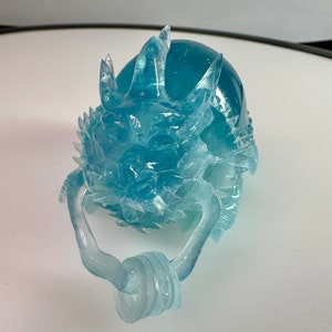 May include: A translucent blue glass dragon sculpture with a curled tail and a detailed face. The dragon is sitting on a white surface.