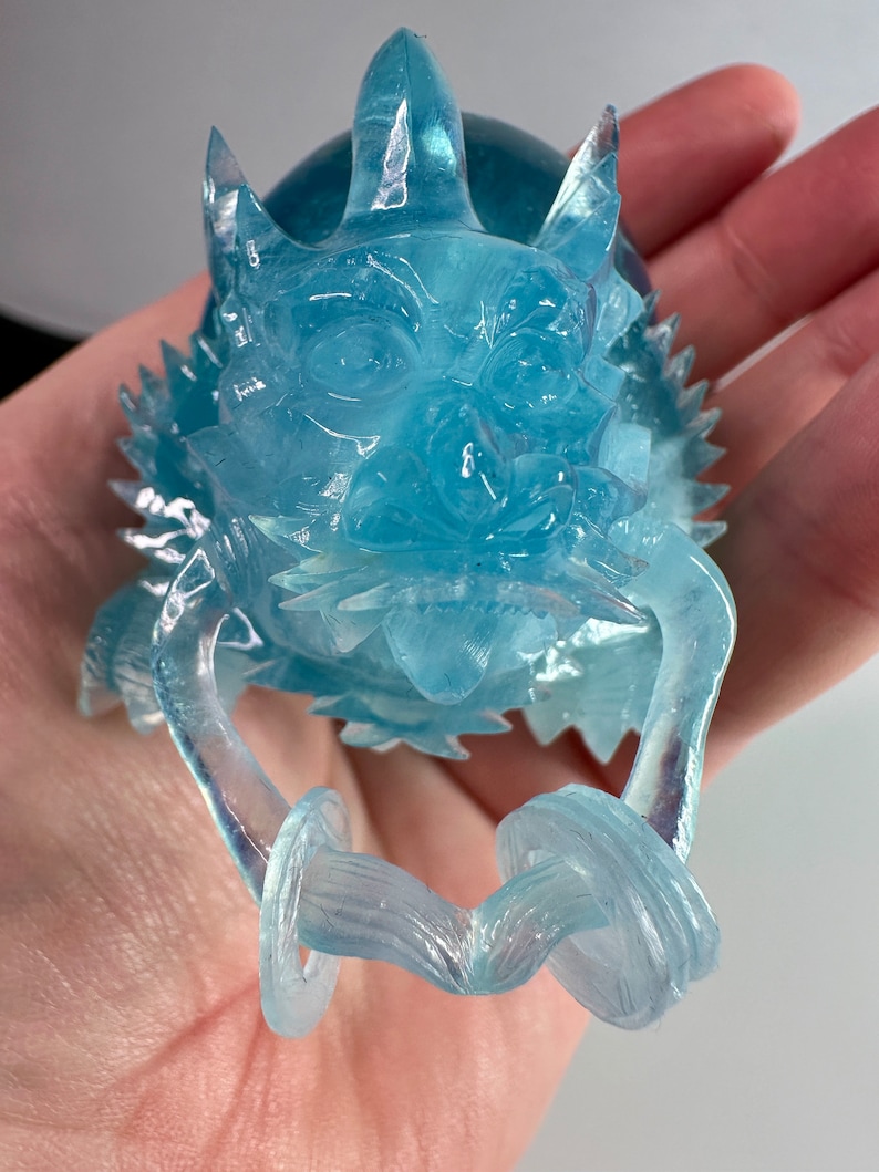 May include: A translucent blue dragon figurine with a detailed face and curled tail. The dragon is made of a clear resin material and has a iridescent finish.