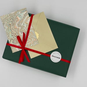 May include: A dark green gift box tied with a red ribbon, topped with a marbled card and a gold envelope. A white sticker with the text "decoriolab" is on the ribbon.